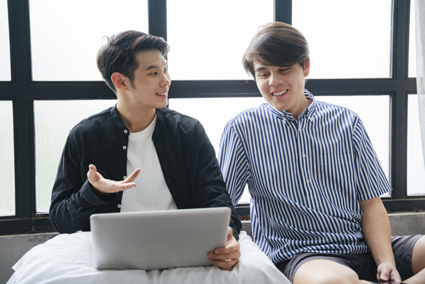 Paar asiatischer LGBTQ + Männer sitzen zusammen und unterhalten sich, während sie Laptop benutzen. - Foto, Bild