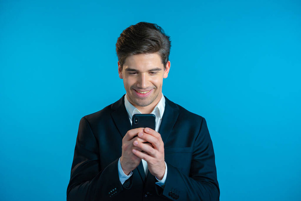 Handsome business man receives happy notification on mobile phone. Guy is beside himself with surprise and joy. He won and rejoices. Technology, success, victory, happiness concept. - Φωτογραφία, εικόνα