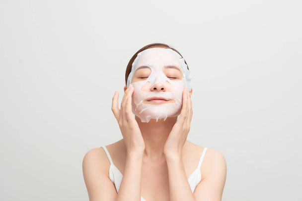 Beautiful asian woman applying paper sheet mask on her face white background - Fotoğraf, Görsel