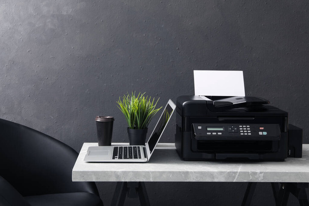 New modern printer, laptop and cup of drink on grey table indoors - Foto, imagen