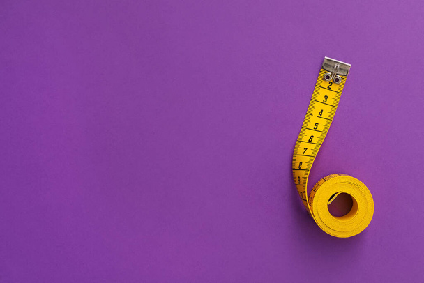 Yellow measuring tape on purple background, top view. Space for text - Fotó, kép