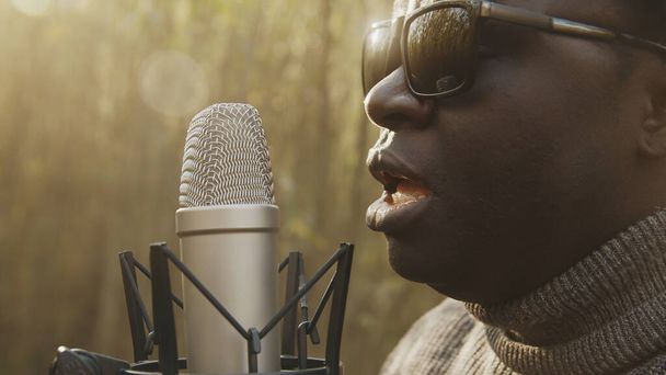 Portré kép afro-amerikai fekete emberről, aki az erdőben énekel a mikrofonban. Természetes fény - Fotó, kép