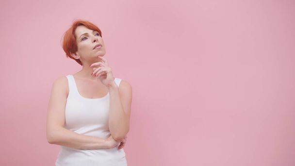 Beautiful redhead woman in white sweatshirt isolated on pink background. Thinking and brainstorming concept - Фото, изображение