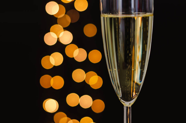 Partial focus of a glass of sparkling wine with golden bokeh lights on dark background. - Photo, Image