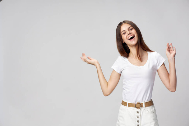 Gestos de mulher feliz com as mãos em uma camiseta branca e em shorts botões de cinto bege  - Foto, Imagem