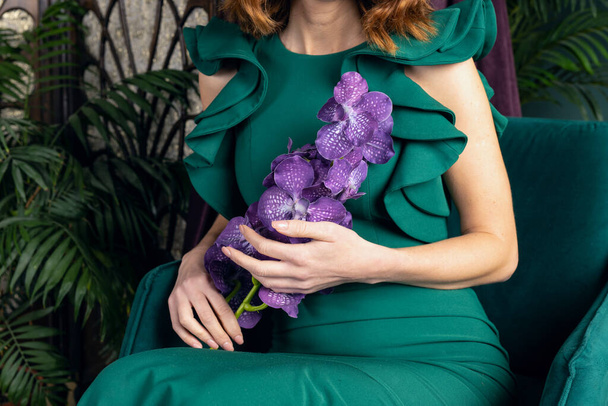 Girl in dress with flowers on green wall background. Sits with closed eyes. - Foto, afbeelding