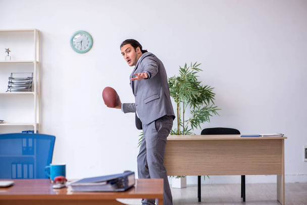 Joven empleado masculino con pelota de rugby en la oficina - Foto, imagen