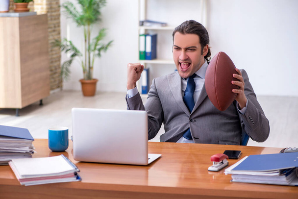 Jeune employé masculin avec ballon de rugby au bureau - Photo, image