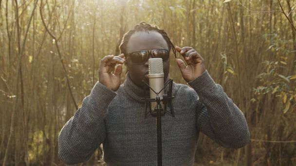 Giovane uomo affricano che canta nella natura, raggi di sole che attraversano gli alberi - Foto, immagini
