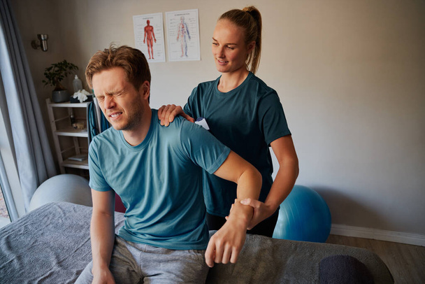 Handsome young male patient suffering from hand injury exercising with female physiotherapist - Photo, image