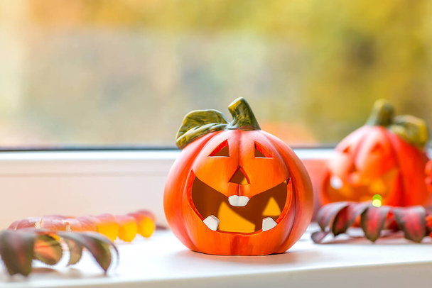 Funny decorative pumpkins for Halloween stand on the windowsill. Outside the window, autumn landscape, bokeh. Selective focus. - Fotó, kép