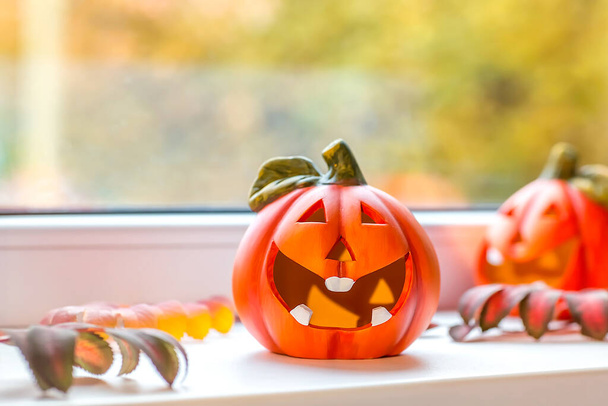 Funny decorative pumpkins for Halloween stand on the windowsill. Outside the window, autumn landscape, bokeh. Selective focus. - 写真・画像