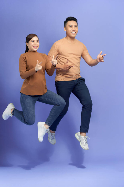 Photo of happy young loving couple jumping isolated over purple background showing thumbs up. - Fotó, kép