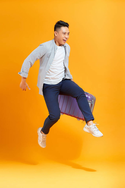Young creative man is posing with suitcase on yellow background. - Photo, image