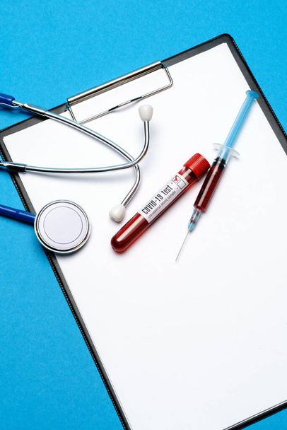 Healthcare concept - Covid-19 positive blood test tube, stethoscope, syringe and clipboard with blank sheet - 写真・画像
