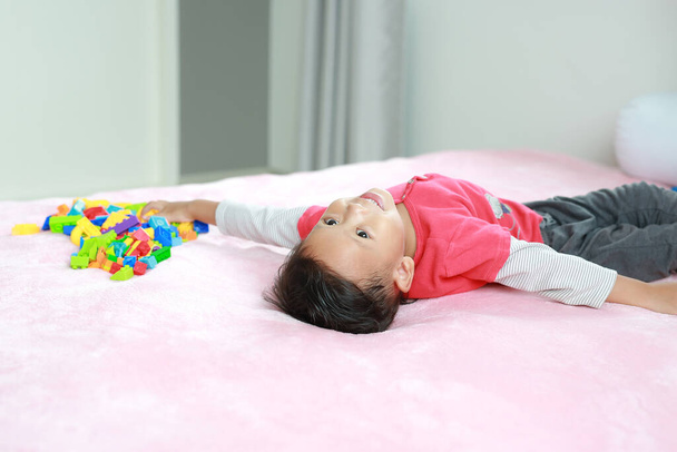 Adorable asian little baby boy playing colorful plastic blocks and lying on bed. - Photo, image