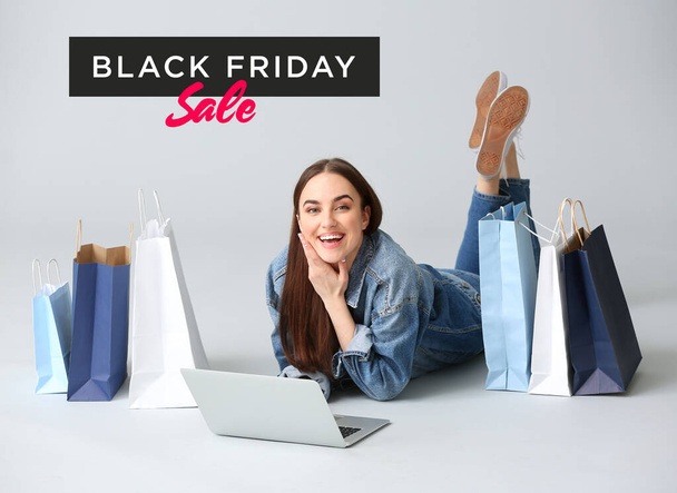 Young woman with laptop and shopping bags on grey background. Black Friday sale - Foto, Imagem