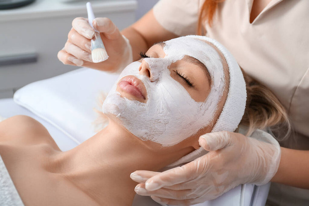 Cosmetologo che applica la maschera su faccia di donna in salone di bellezza - Foto, immagini