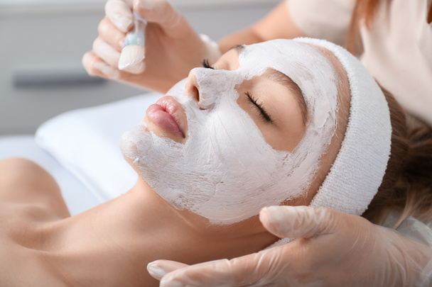 Cosmetoloog aanbrengen van masker op gezicht van vrouw in schoonheidssalon - Foto, afbeelding