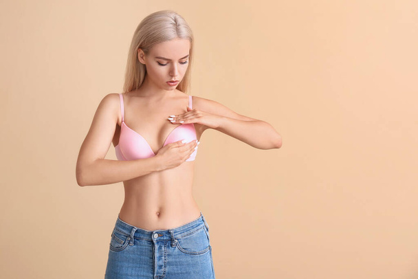 Junge Frau überprüft ihre Brust auf farbigem Hintergrund. Krebsaufklärungskonzept - Foto, Bild