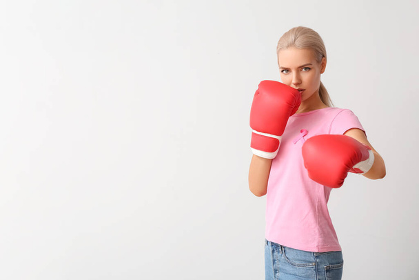 Mladá žena v boxerských rukavicích na šedém pozadí. Koncepce povědomí o rakovině prsu - Fotografie, Obrázek