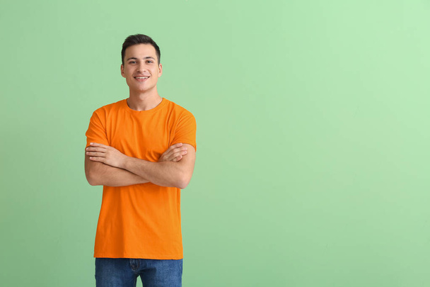 Красивый молодой человек в оранжевой футболке на цветном фоне - Фото, изображение
