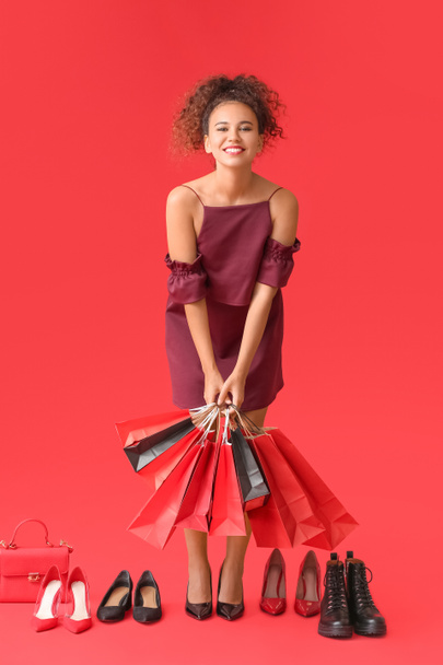 Hermosa mujer afroamericana con bolsas de compras y zapatos en el fondo de color. Viernes Negro venta - Foto, Imagen