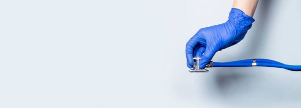 Hand in glove holding stethoscope on blue background, banner with copy space. - Foto, imagen