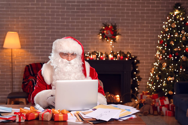 Санта-Клаус с ноутбуком проверяет электронную почту дома в канун Рождества - Фото, изображение