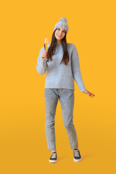 Beautiful young woman in winter clothes and with champagne on color background - Photo, Image