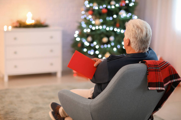 Olgun bir adam Noel arifesinde evde kitap okuyor. - Fotoğraf, Görsel