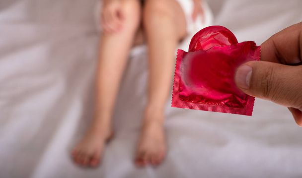 Чоловік показує червоний презерватив жінці з рушником лежить в ліжку, безпечний секс і охорона здоров'я і медична концепція
 - Фото, зображення