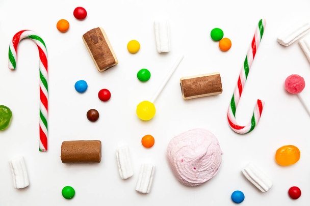 Varios dulces de colores sobre un fondo blanco. Piruletas, caramelo, bastones de caramelo, malvaviscos, chocolate, galletas vista superior - Foto, imagen