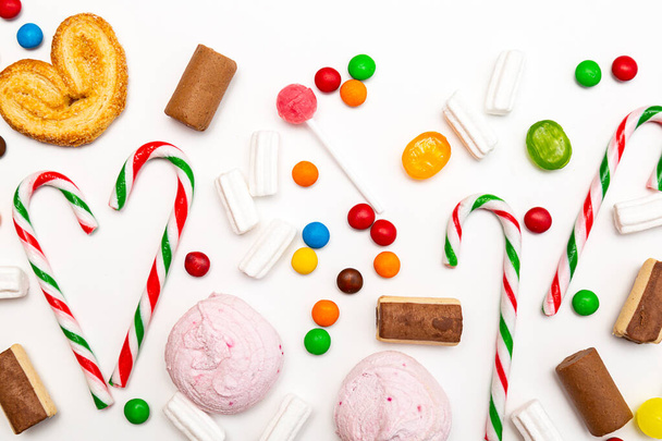 Diverse gekleurde snoepjes op een witte achtergrond. Lollipops, karamel, zuurstokken, marshmallows, chocolade, koekjes bovenaanzicht - Foto, afbeelding
