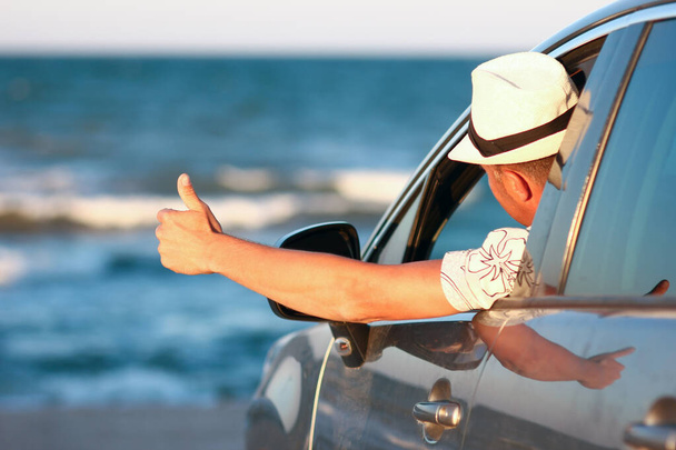 Happy guy in the car by the sea in nature on vacation travel - Photo, image