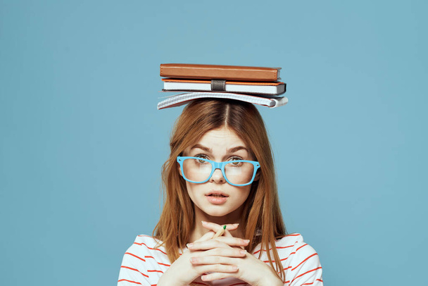 Female student with books on her head science education blue background emotions gesturing with hands - Fotoğraf, Görsel