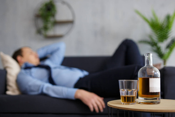 alcoholismo, estrés y concepto de negocio - primer plano de botella de whisky y vidrio en la mesa y dormir hombre de negocios borracho - Foto, Imagen
