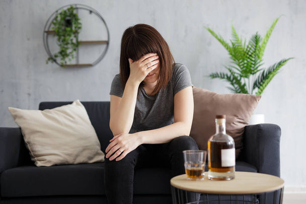 alcoholism and depression concept - young stressed woman drinking alcohol at home - Photo, image