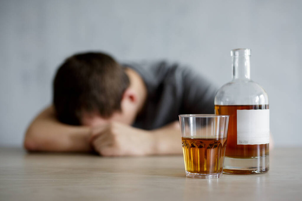 alcoholismo y depresión concepto - primer plano de vidrio y botella de whisky y hombre borracho acostado en la mesa - Foto, Imagen