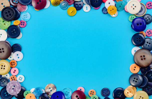 A pile of multicolored sewing buttons on blue background. Tailoring concept. Flat lay. Empty place for text. - 写真・画像