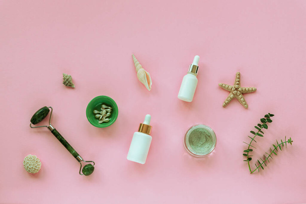 Natural organic beauty skincare products. Serum, cream jar, beauty capsules, face roller, seashell and eucalyptus sprig - Photo, Image