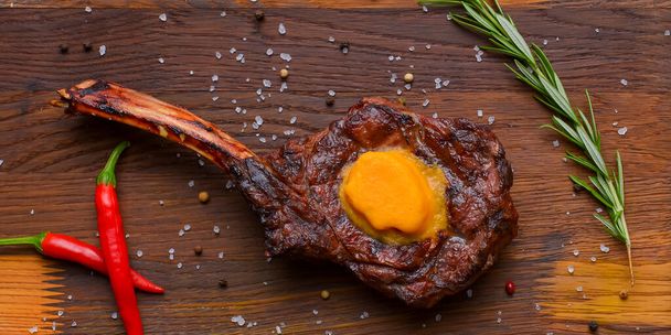 Barbecue tomahawk steak with spices served on a rustic wooden board over wooden background. BBQ concept, grilled meat steak, autumn seasonal dish. - Foto, imagen