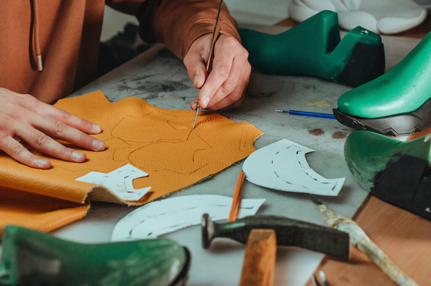 Schoenmaker snijden patronen met behulp van mes van leer in zijn werkplaats. - Foto, afbeelding