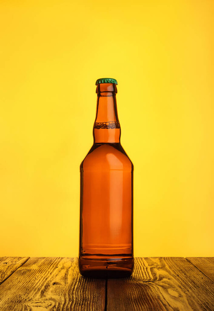 Glass bottle of fresh beer on dark wood against yellow background. - Fotografie, Obrázek