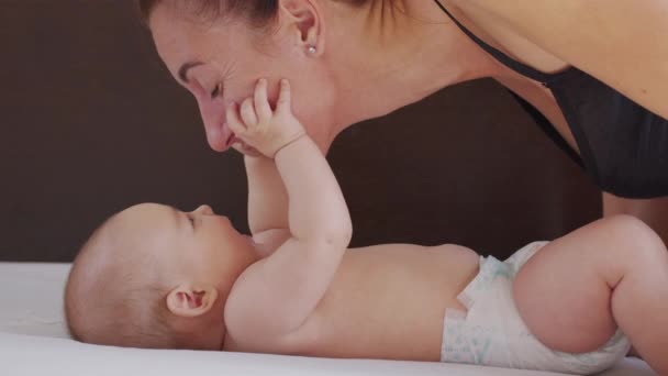 Nahaufnahme. Mutter küsst Baby sanft und genießt liebevolle Mama, die sich zu Hause spielerisch um ihr Kleinkind kümmert und die Verbindung mit ihrem Neugeborenen teilt. Gesunde Kinderbetreuung. - Filmmaterial, Video