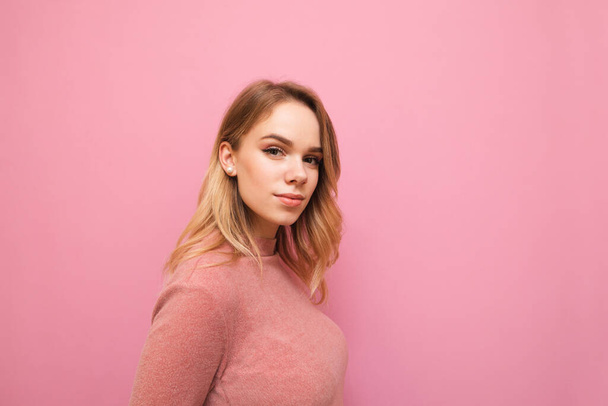 Portrait of attractive blonde woman in pink sweater isolated on pink background looking into camera with serious face. Pretty lady posing at camera against pink wall background. - Фото, зображення
