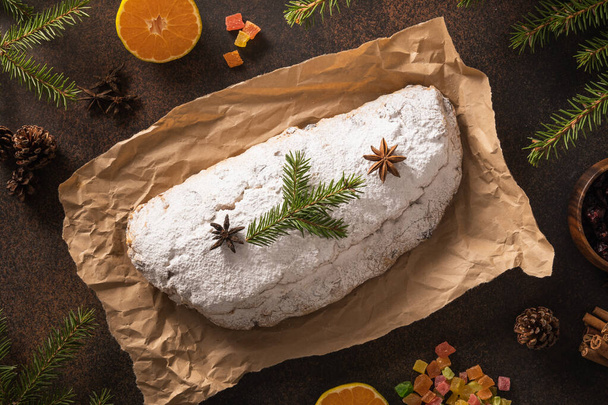 Christmas stollen - traditional German bread decorated fir tree branches and ingredients candied fruit on brown background. Holiday pastry dessert. View from above. - Photo, Image
