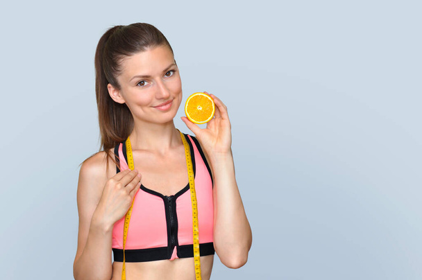  Athletic young woman in a pink top holds half an orange. - Foto, Bild