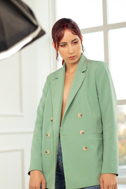 retrato de uma jovem com cabelo vermelho com maquiagem e em uma jaqueta verde e jtns no estúdio, moda - Foto, Imagem