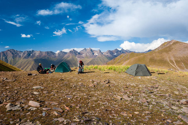 Group of trekkers camping in mountain pass. Climbers pitch tent in nature near Sary Chelek lake, Sary-Chelek Jalal Abad region, Kyrgyzstan, Trekking in Central Asia. - Photo, Image